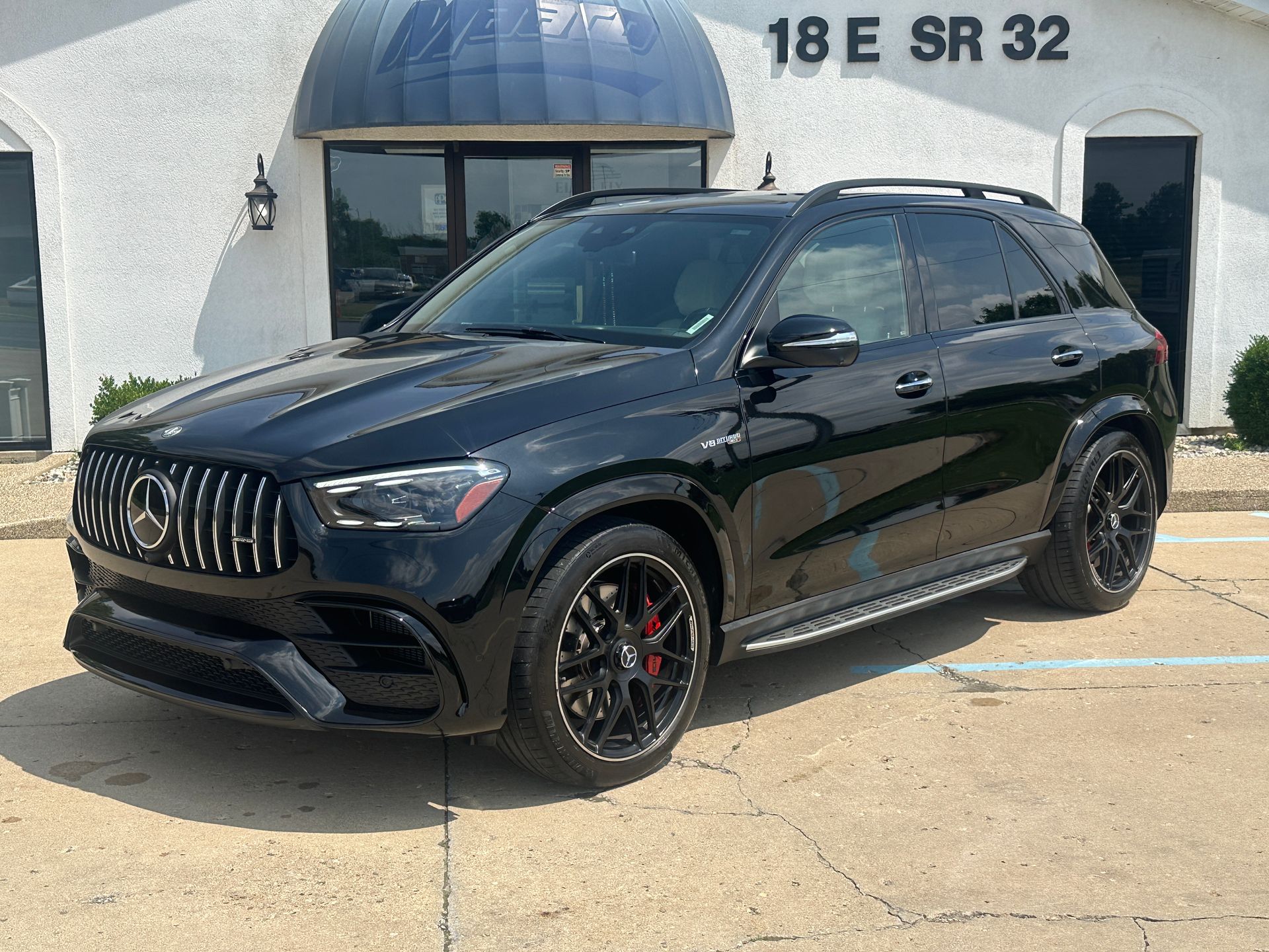 Black Mercedes-AMG SUV parked in front of a building with a blue awning and a street number.