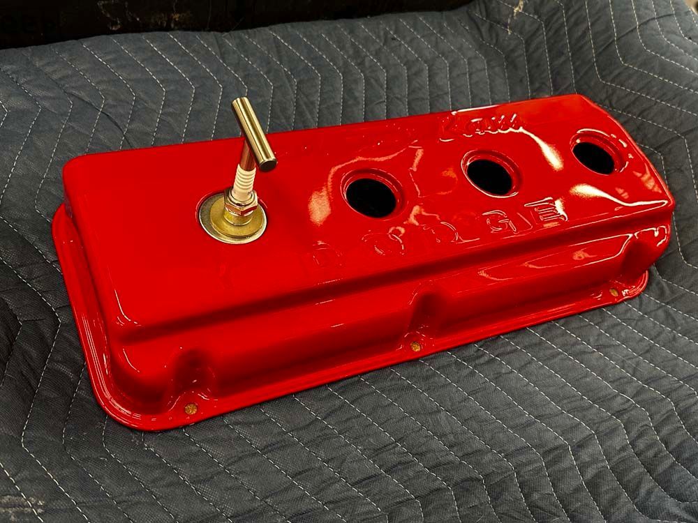 A red valve cover with holes in it is laying on a blanket