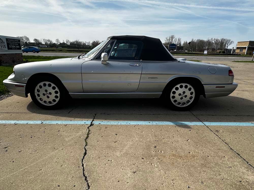 A silver car with a black top is parked in a parking lot.