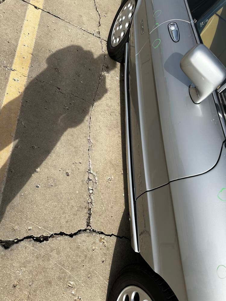 A silver car is parked in a parking lot with its shadow on the ground