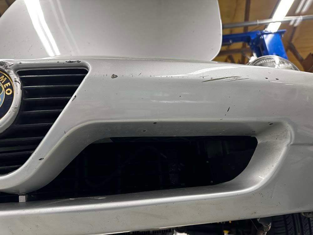 A white car with a damaged bumper is sitting on a lift in a garage.