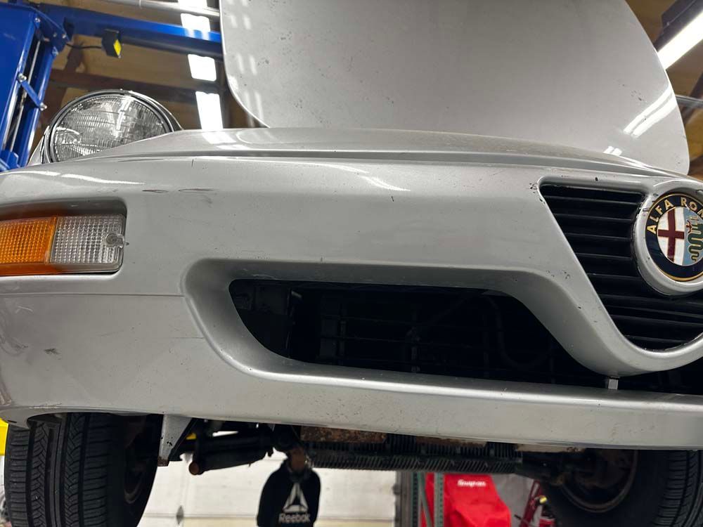 The front end of a white alfa romeo with the hood open.