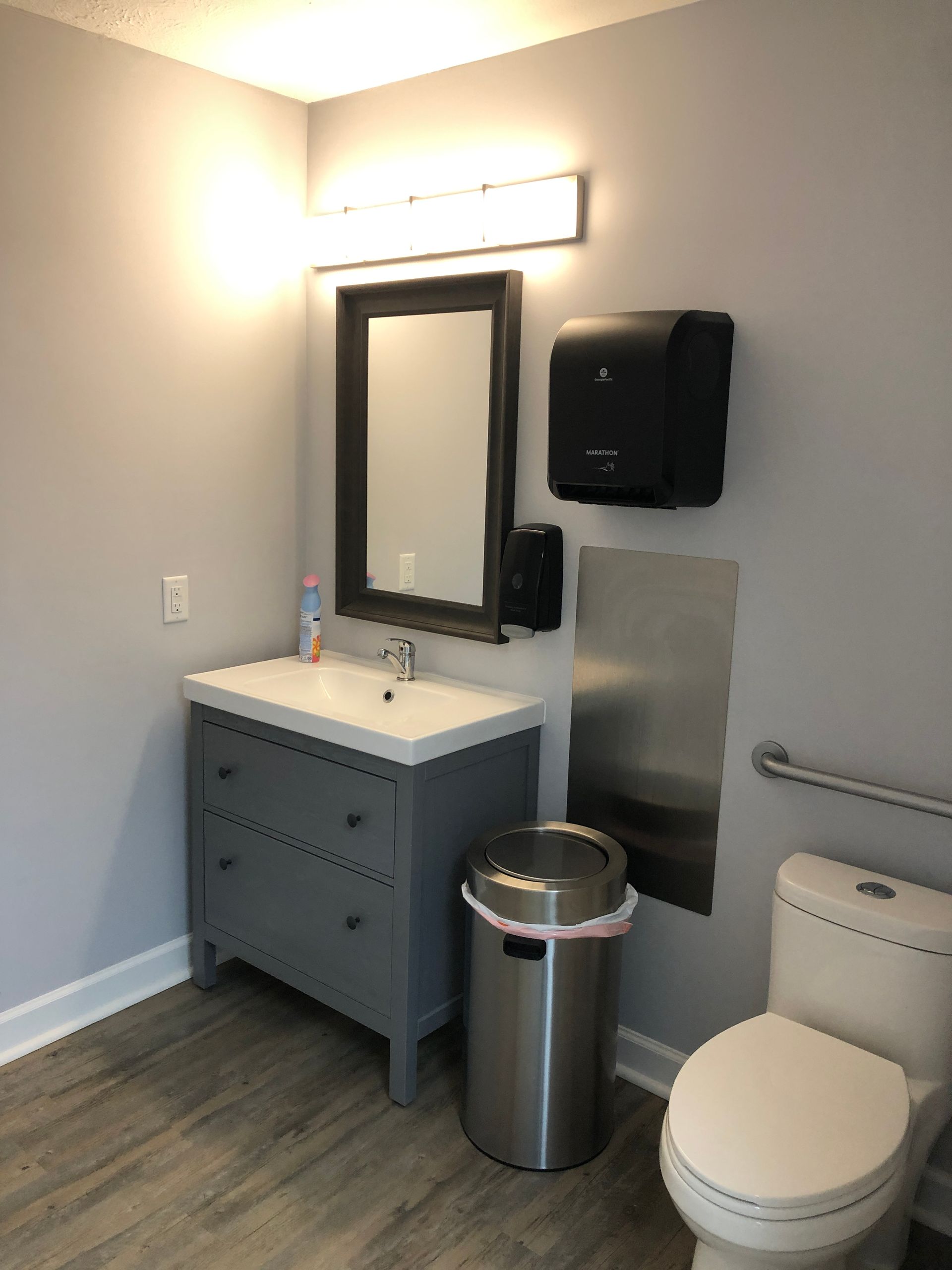 A bathroom with a sink , toilet , trash can and mirror.