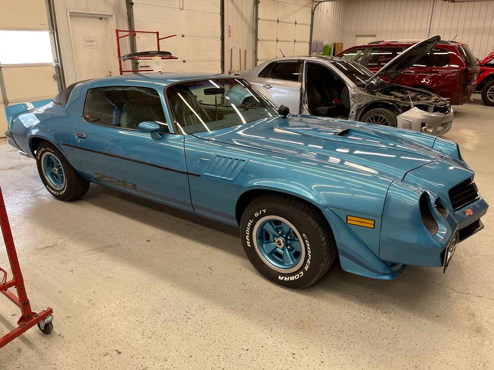 A blue car is parked in a garage next to another car.