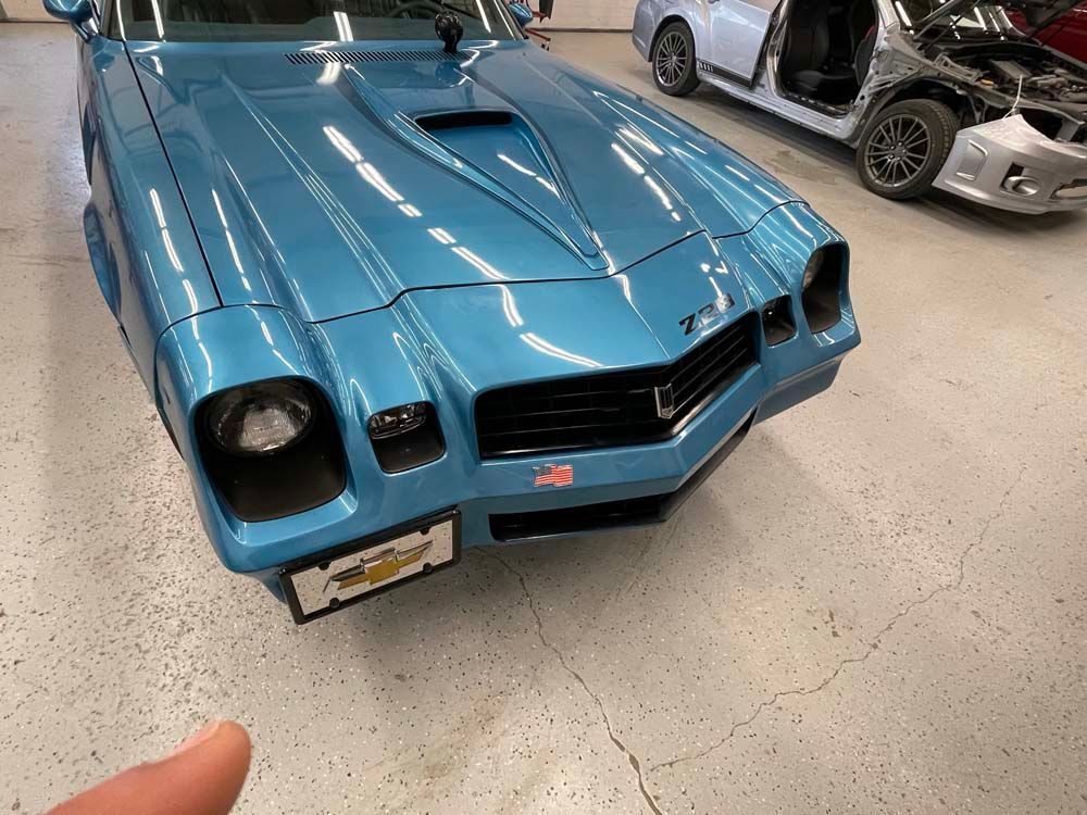 A blue car is parked in a garage next to another car.