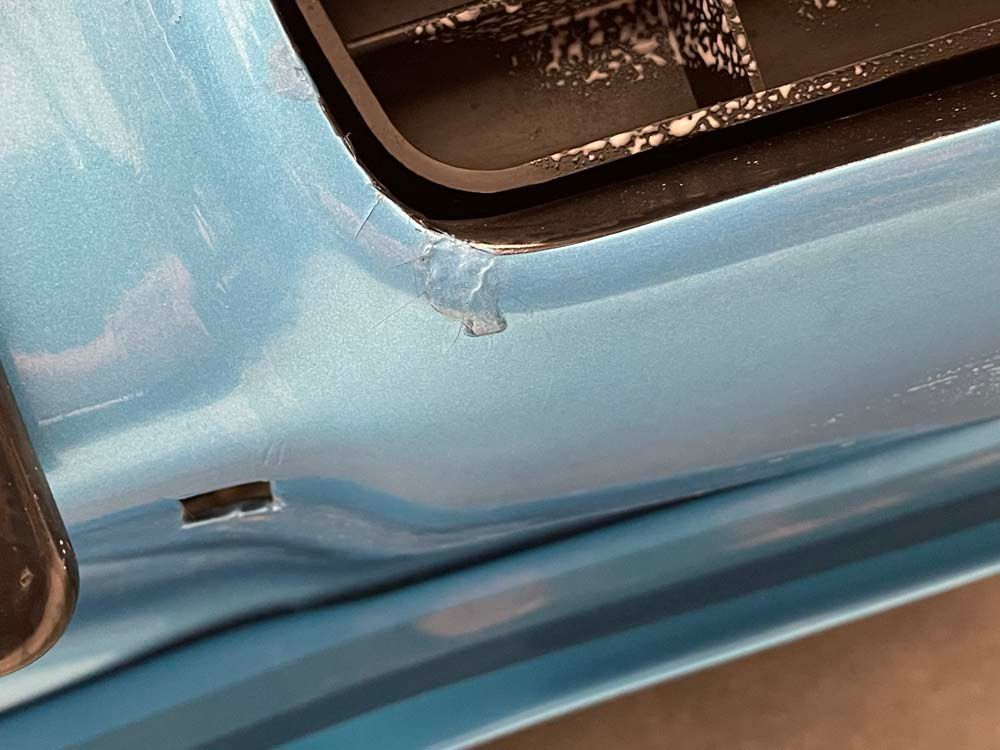 A close up of a blue car with a scratch on the side.