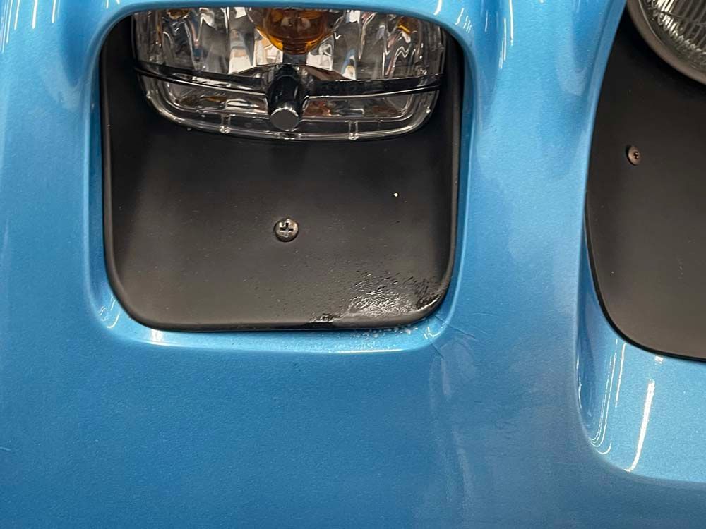 A close up of a blue car 's headlight and bumper.