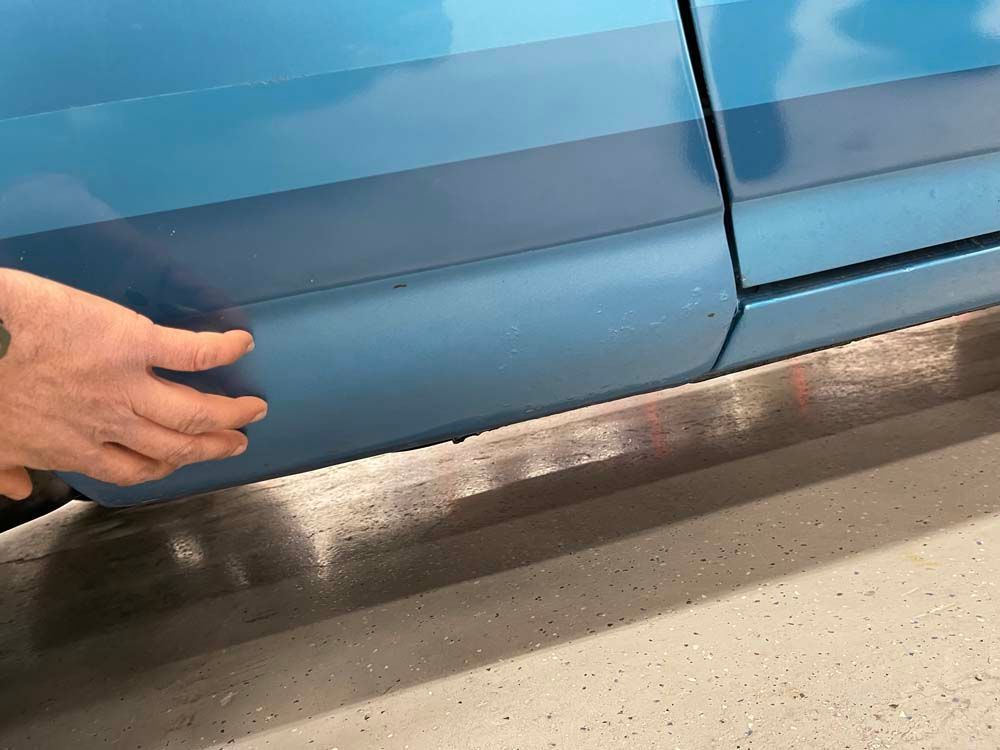 A person is touching the side of a blue car
