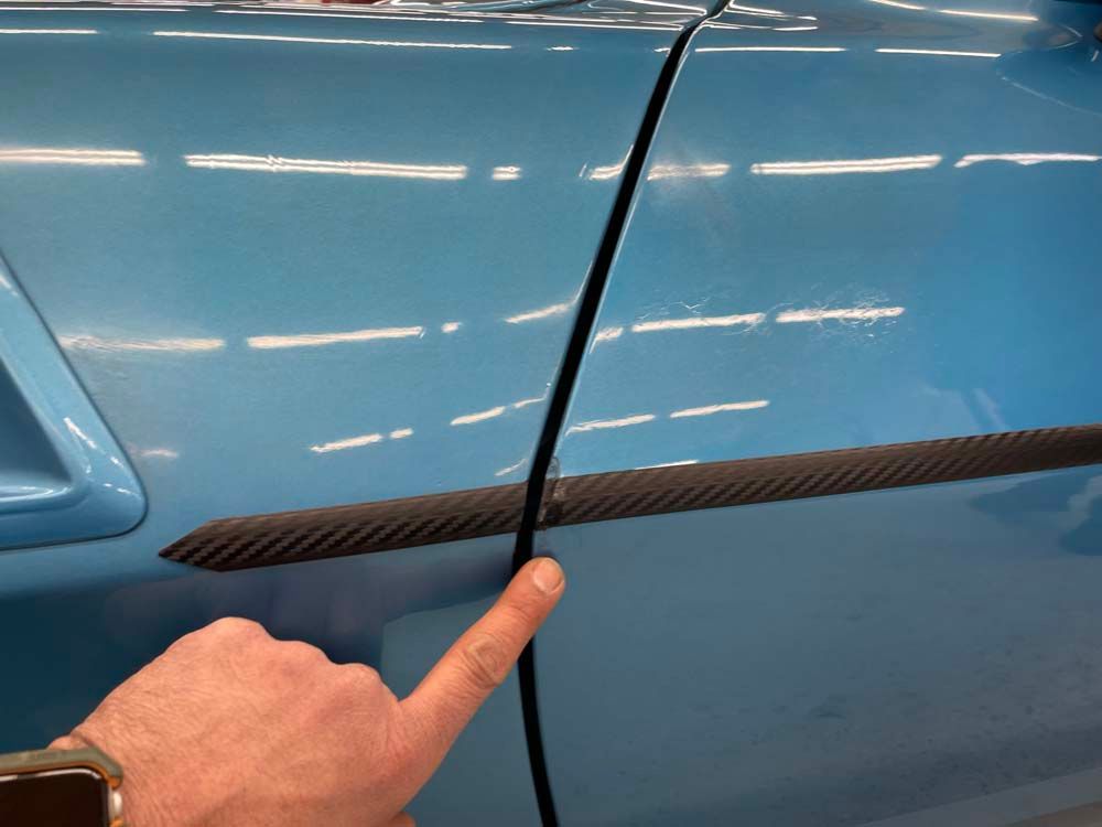 A person is pointing at the side of a blue car