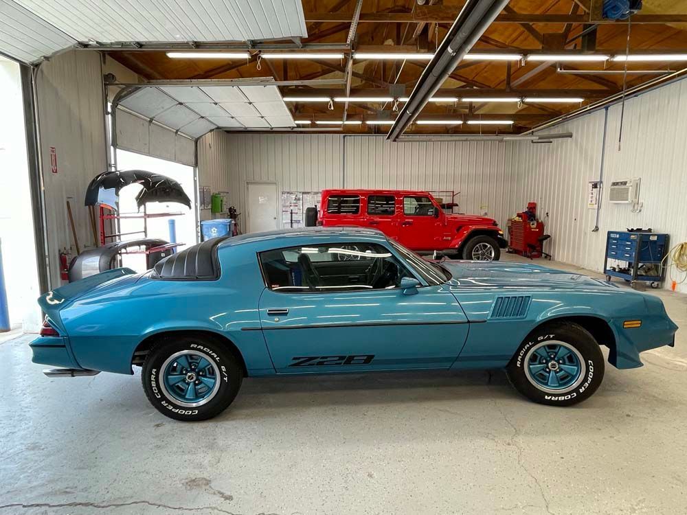Blue 1970s Z/28 Camaro in a garage, with a red Jeep behind it.
