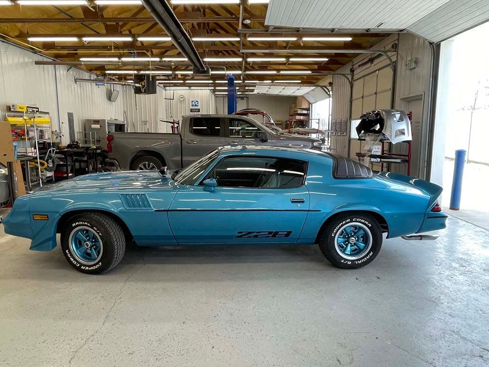 A blue car is parked in a garage next to a truck.