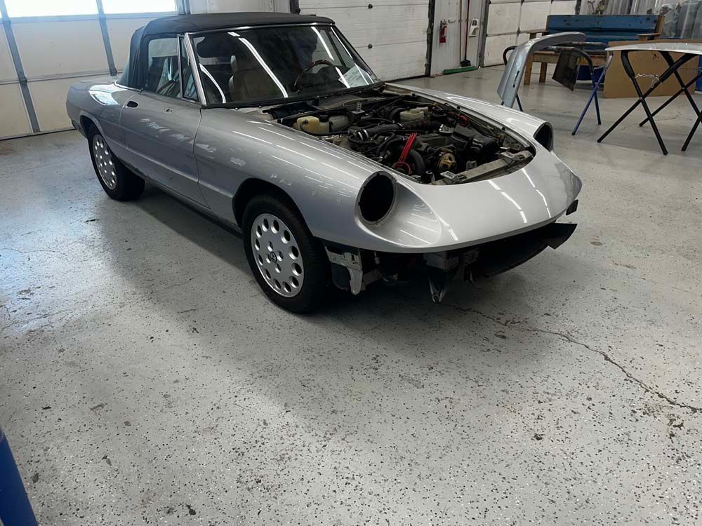 A silver car with the hood up is parked in a garage.