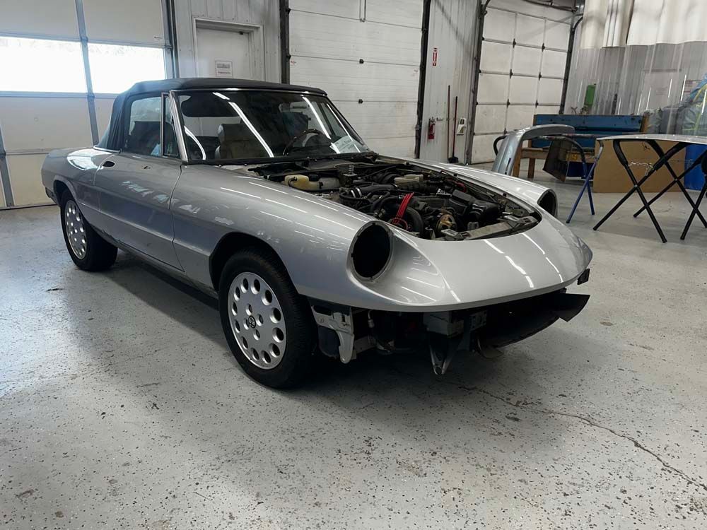 A silver car with the hood open is parked in a garage.