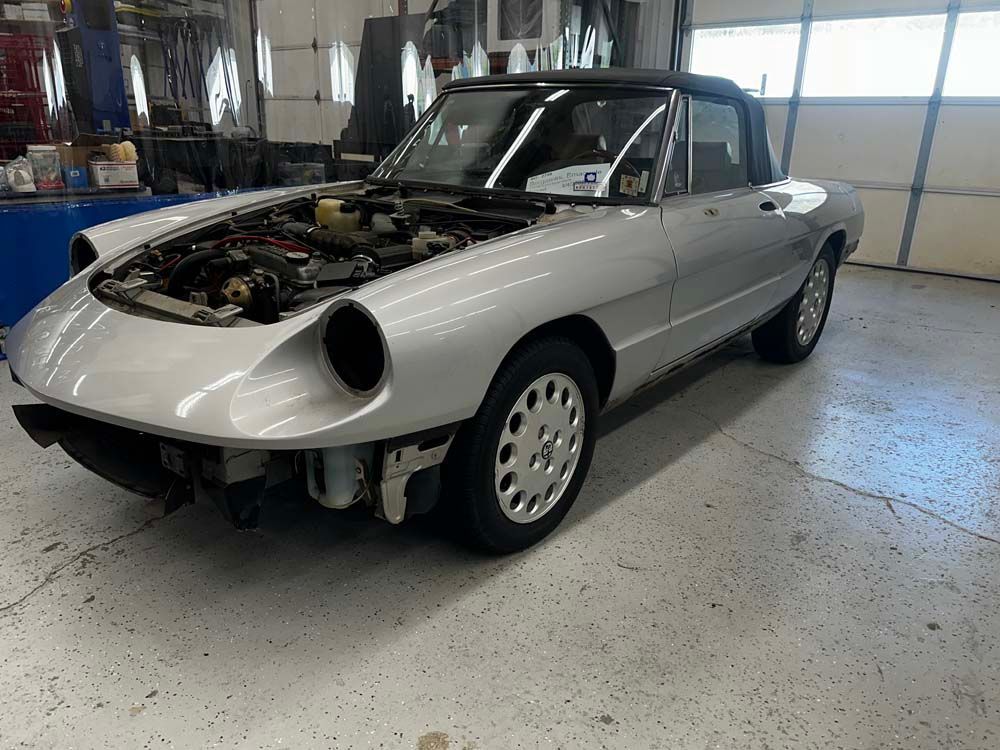 A silver car with the hood up is parked in a garage.