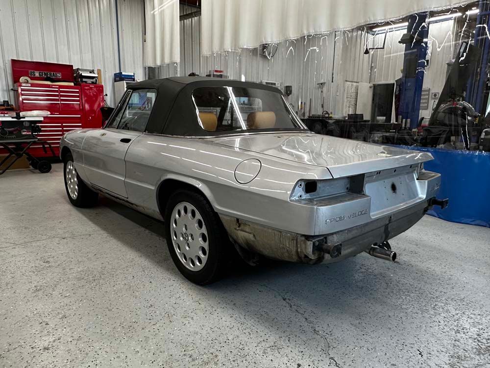 Silver Alfa Romeo convertible in a workshop with the rear bumper removed.