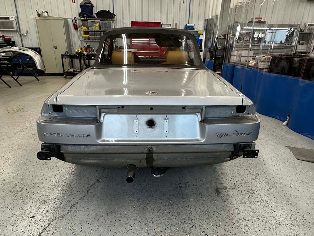 A silver car is sitting in a garage with the trunk open.