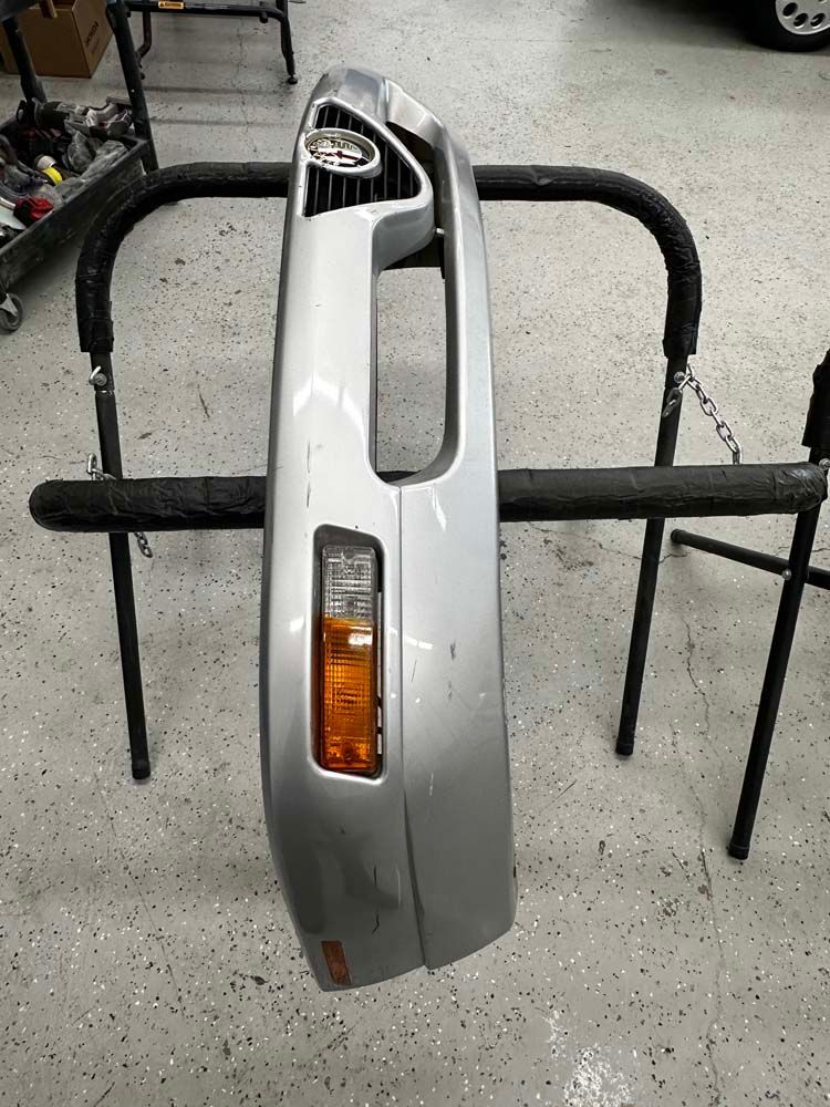 A silver bumper is sitting on a metal stand in a garage.