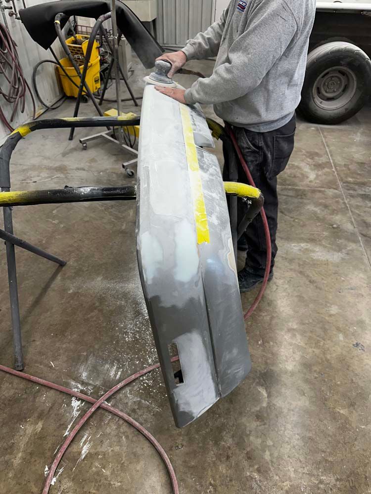 A man is sanding a piece of metal in a garage.