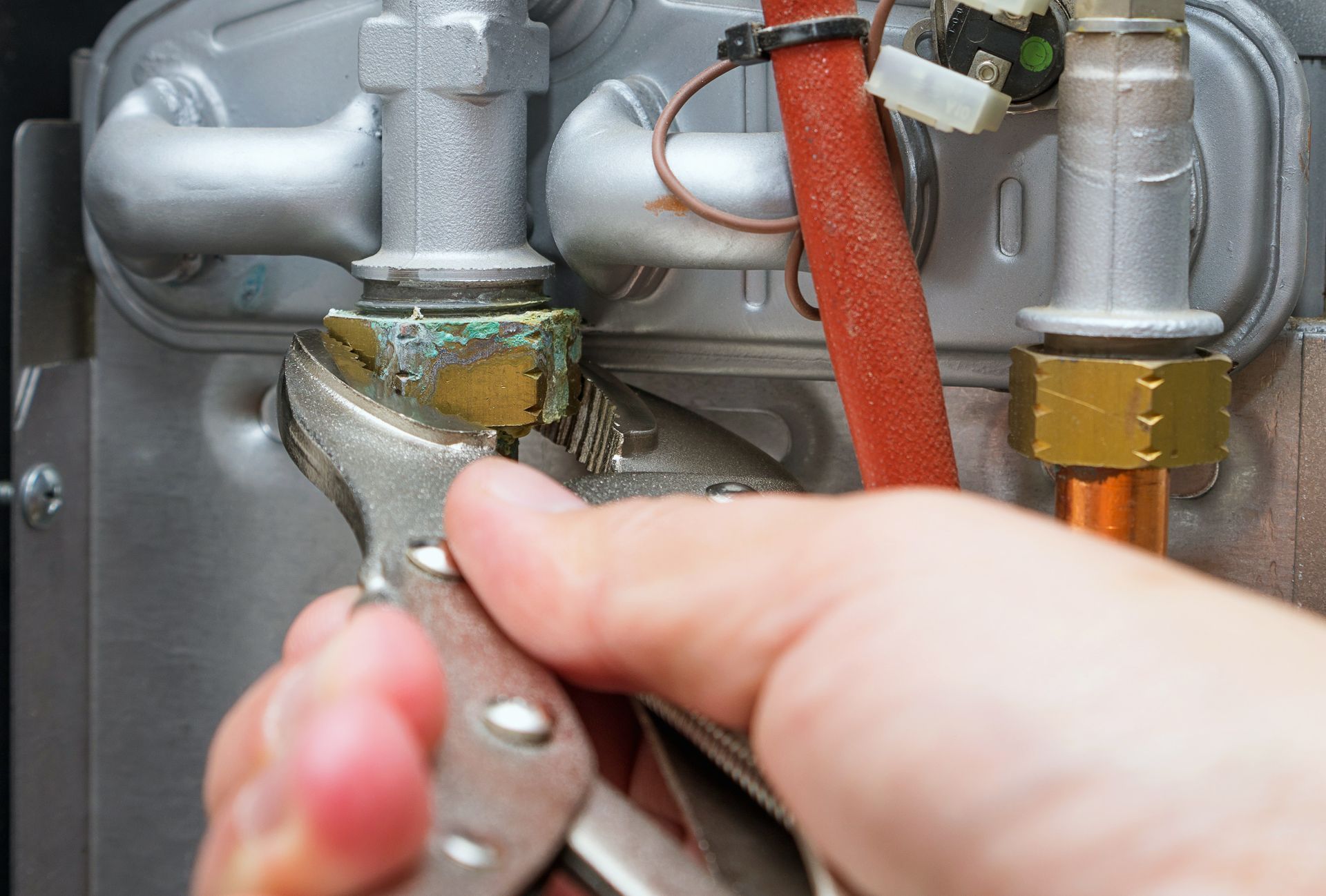 Hand tightening a wrench on a brass pipe fitting beneath a sink or appliance