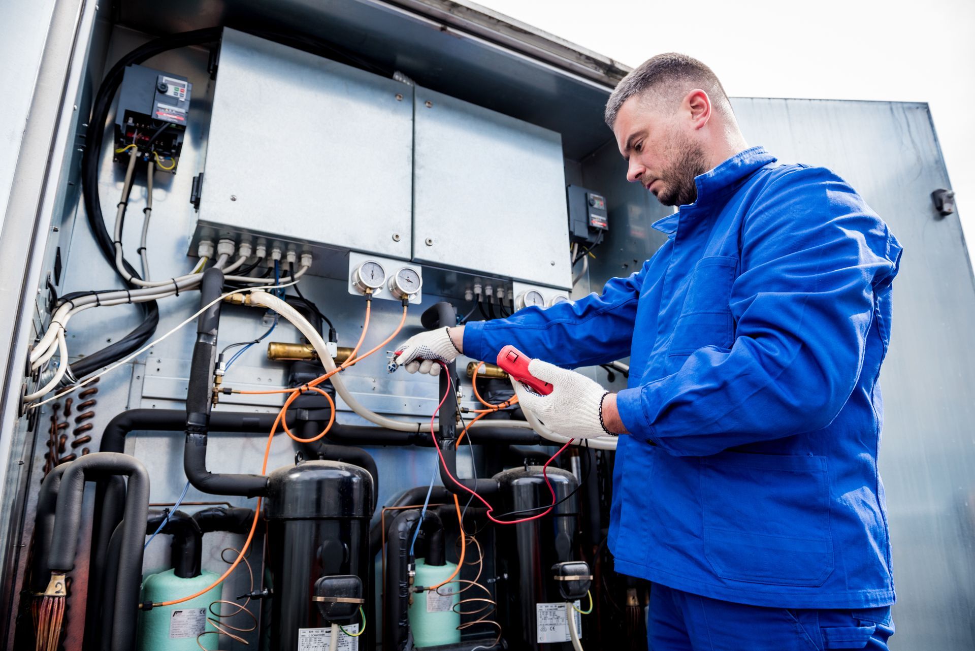 Technician in blue jacket inspecting wiring inside an open electrical cabinet.