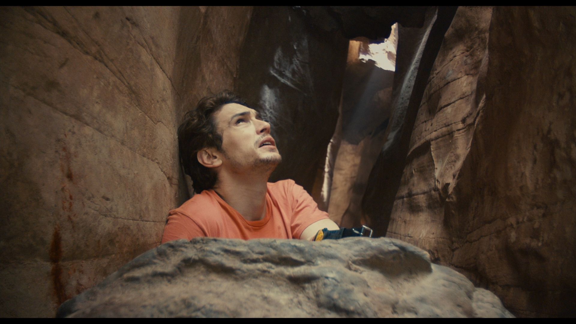 Man trapped in a narrow canyon, looking up with a worried expression. Dark figure looms above, casting a shadow.