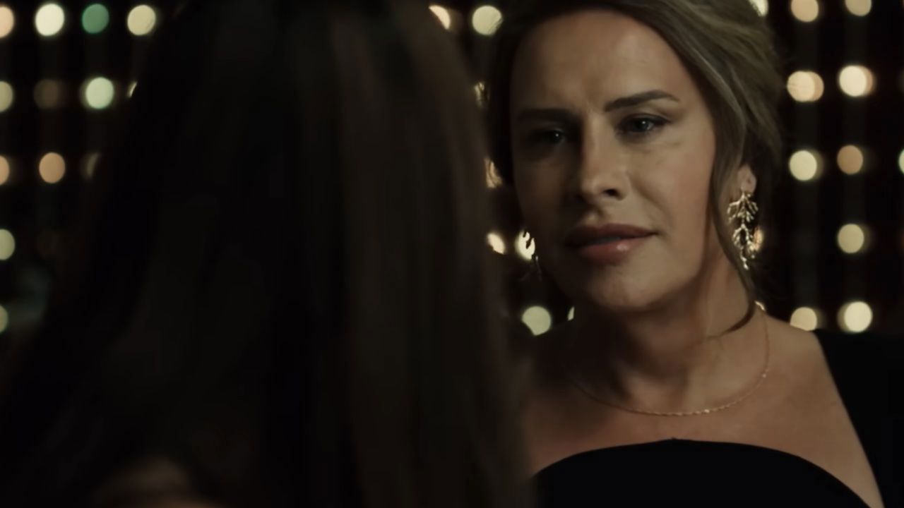 Woman in black dress, talking to someone out of frame, in a dimly lit room with lights.