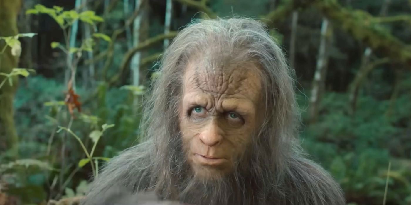 A close-up of a Bigfoot-like creature in a forest; it looks directly at the viewer.