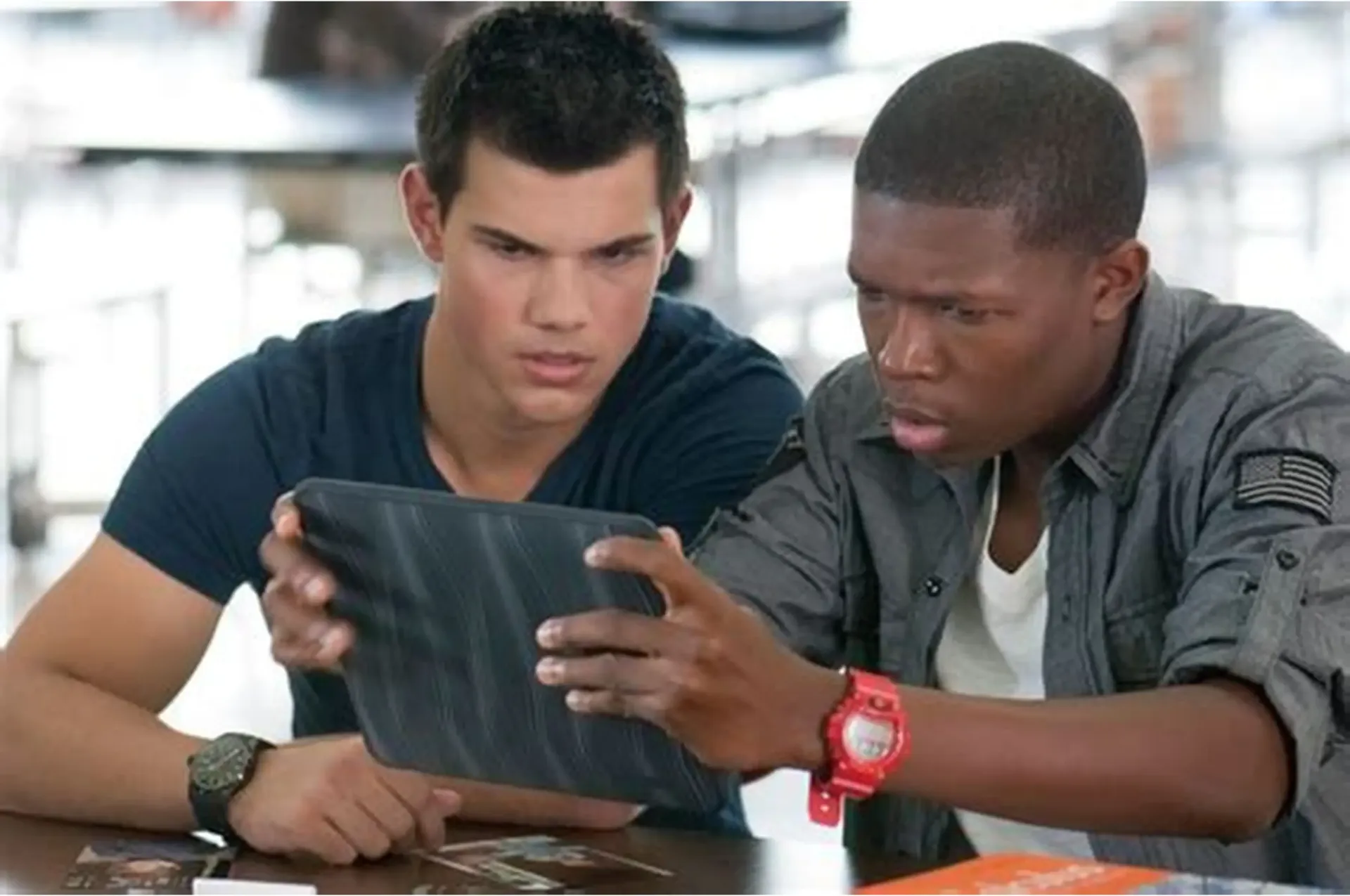 Two young men looking intently at a tablet screen. They are inside, possibly a school, with serious expressions.