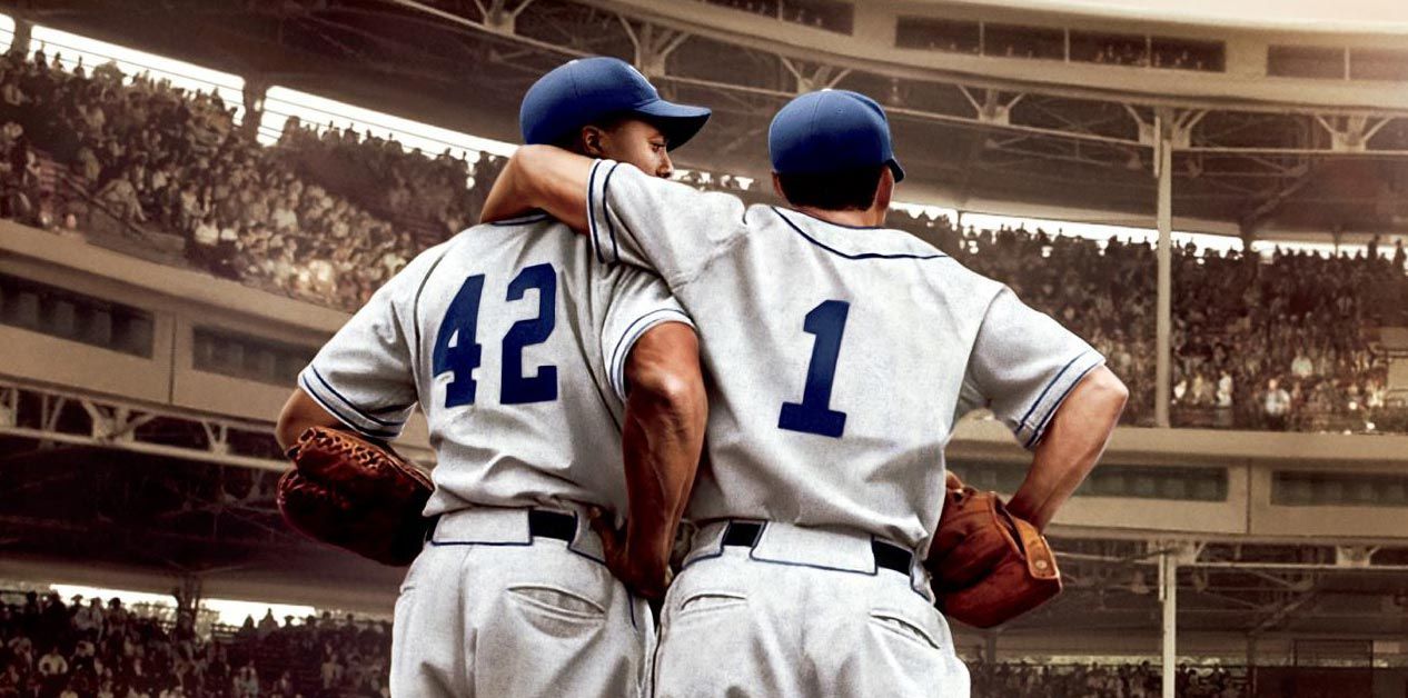 Two baseball players in Brooklyn Dodgers uniforms, arms around each other, looking towards the stadium crowd. One wears number 42, the other number 1.