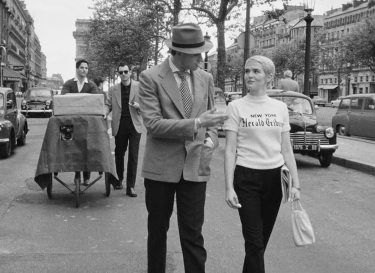 Man and woman walking on a Paris street, man points, a cart and cars in background.