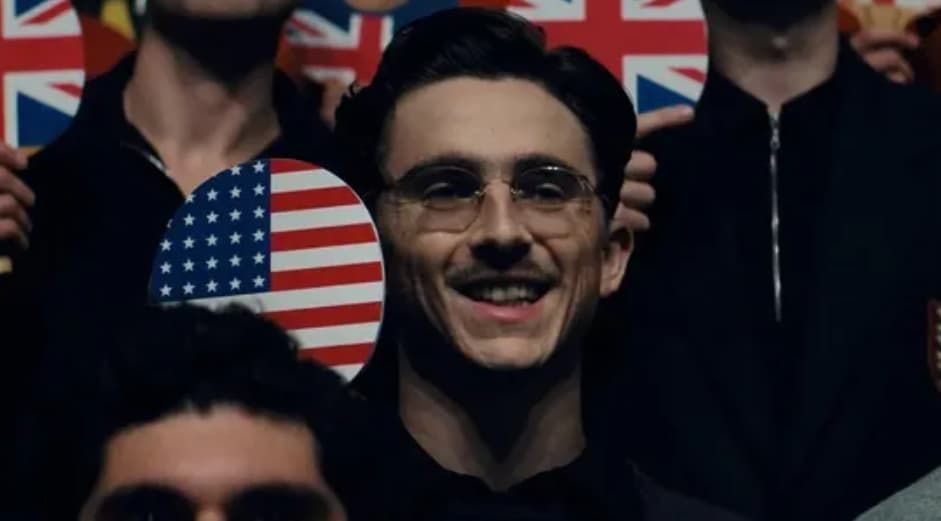 Man smiling, wearing glasses, holding a US flag, surrounded by people with flags.