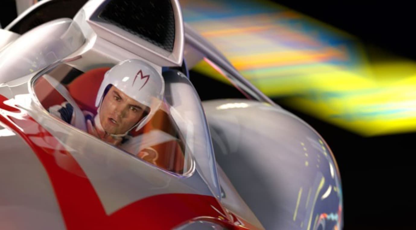 Race car driver in a red-and-silver car, leaning forward with a focused expression on a blurred track