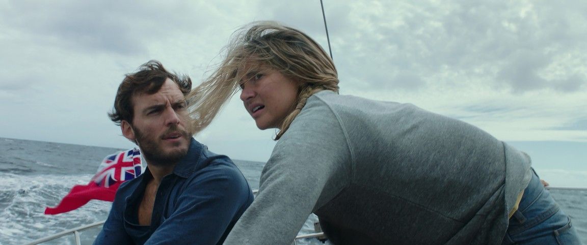 A man and woman on a boat, facing forward. The woman is in motion. They are on the water.
