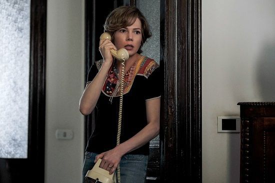 Woman in a doorway, talking on a landline phone. She wears a black top, jeans, and has a surprised expression.