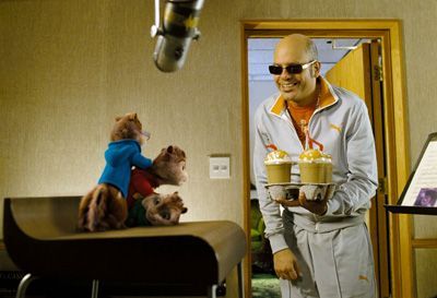 Alvin and the Chipmunks recording in a studio. Dave holds two orange drinks, smiling at the singing chipmunks.