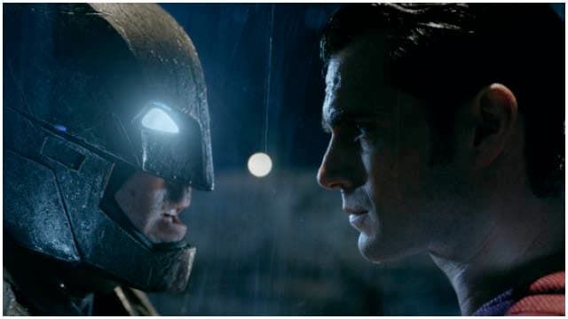 Batman and Superman stand face-to-face in a close-up, dramatic shot under rainy, dark lighting.