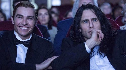 Two men in tuxedos at a movie premiere. One smiles, the other nervously bites his nails.