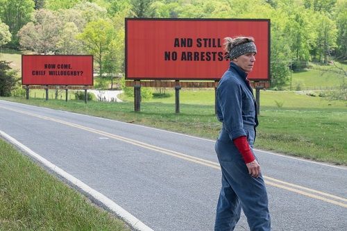 Woman stands on a rural road in front of two red billboards.