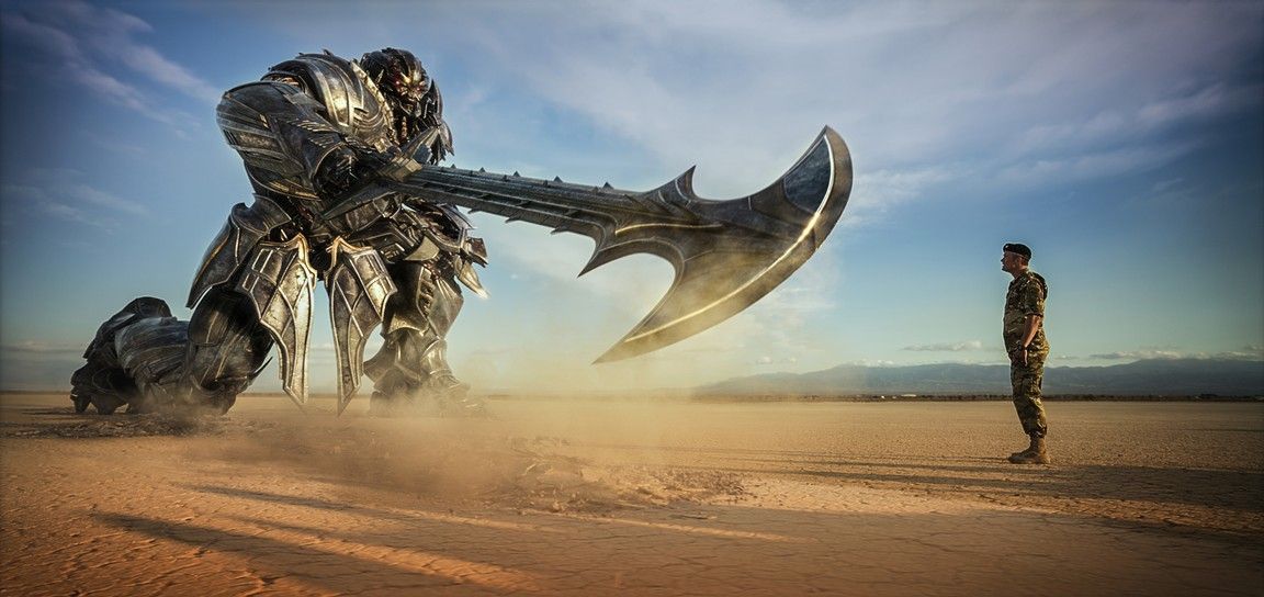 A giant robot with a massive axe faces a soldier in a desert setting under a blue sky.