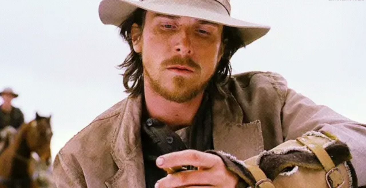 Man in cowboy hat and dusty clothes, looking weary, holding reins in a desert setting.