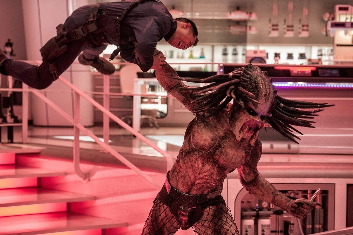 A Predator fighting a man in a brightly lit, modern setting with a red and white color scheme.