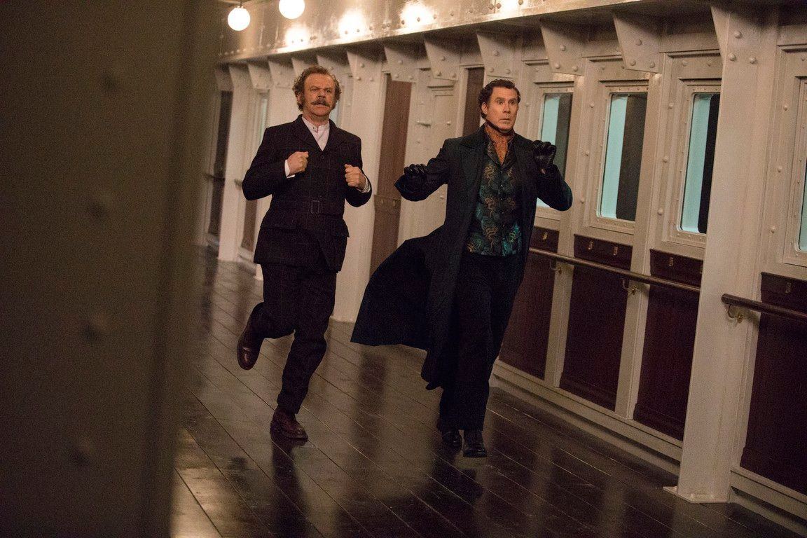 Two men run down a hallway, one in a suit, the other in a long coat.