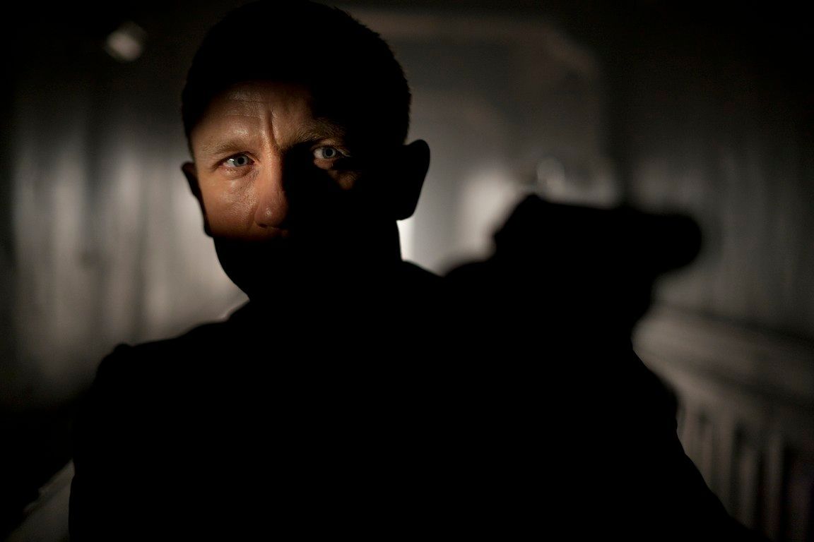 Man in shadow points a gun in a dark hallway; focused on his intense gaze.