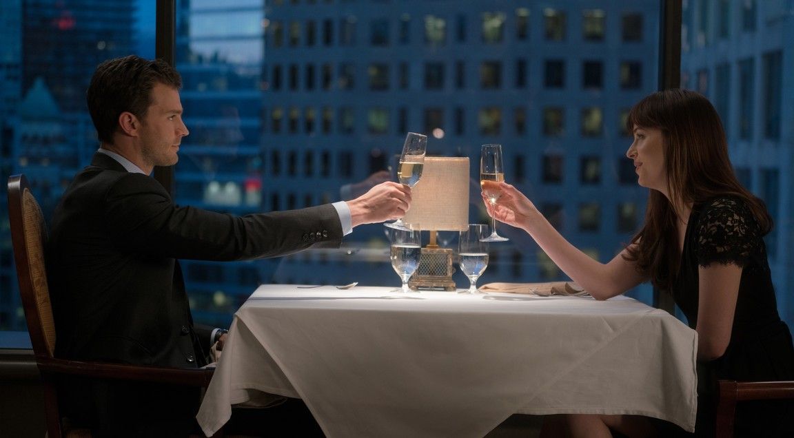 Man and woman toasting with champagne glasses at a fancy restaurant with a city view.