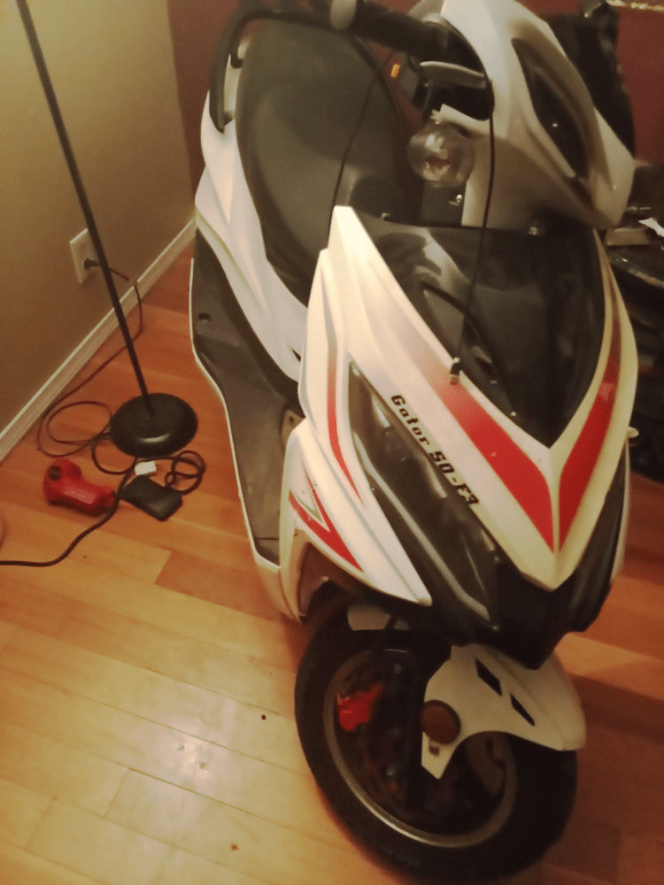White and red scooter parked on a wood floor near a lamp.