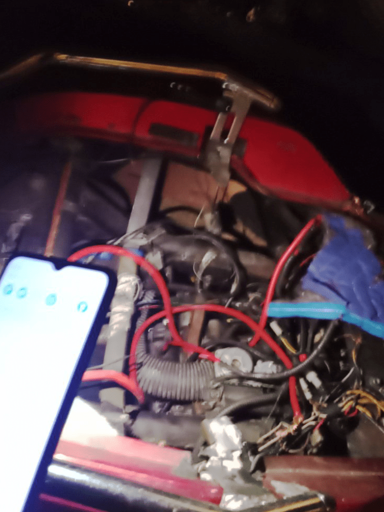 Engine compartment with red wires, smartphone in view.