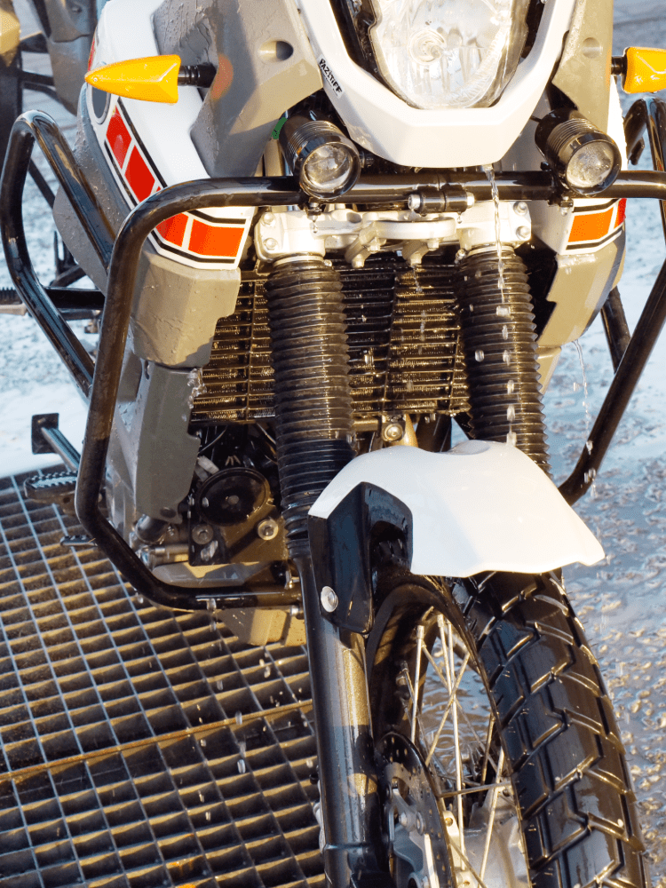 Front view of a white and gray motorcycle with black crash bars, front tire on a metal grate.