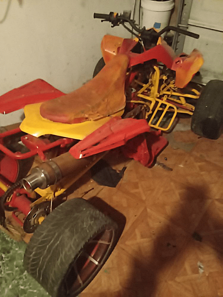 Partially disassembled red and yellow ATV in a room with a brown floor and white bucket.