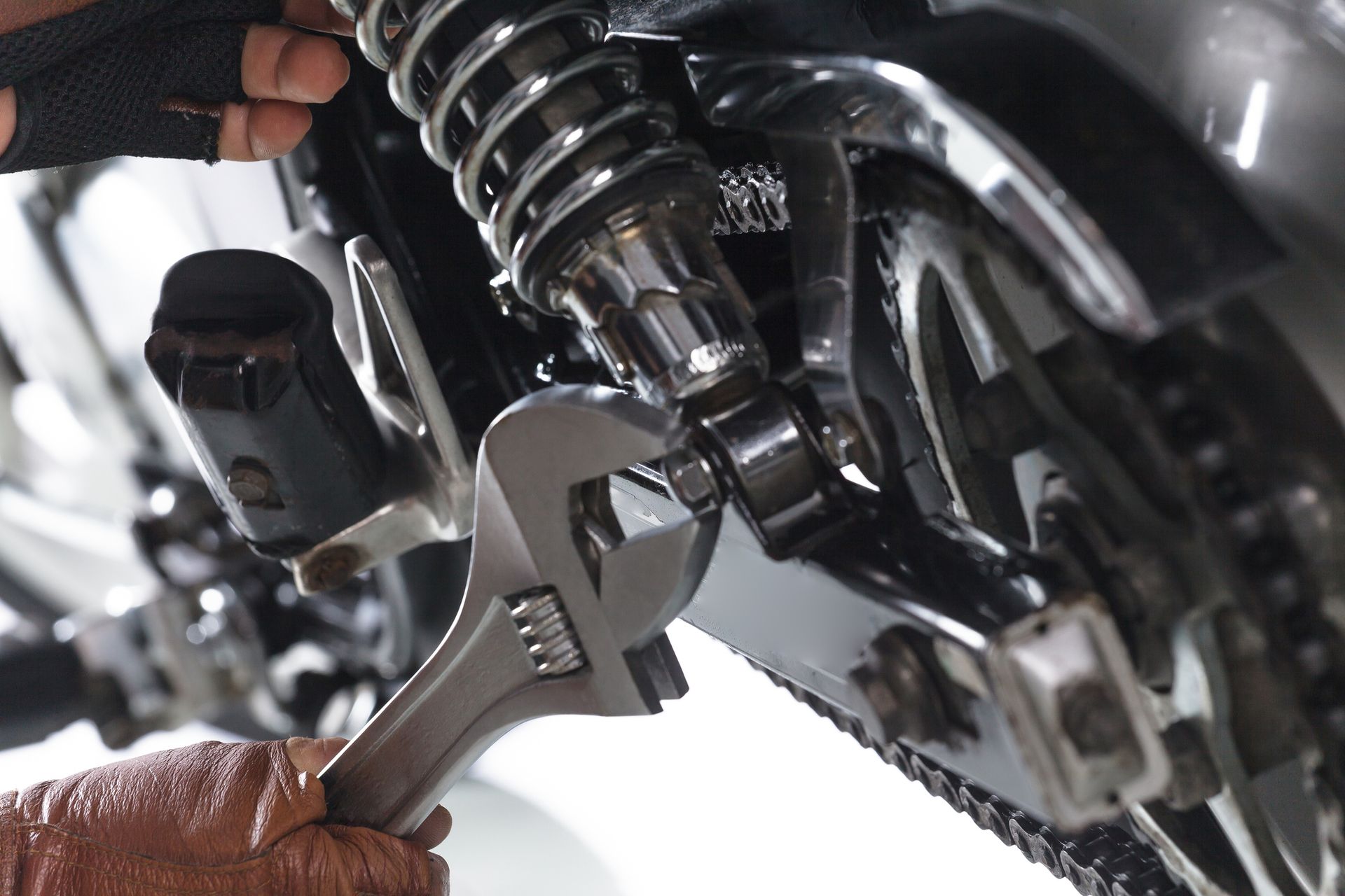 Person using a wrench to tighten a bolt on a motorcycle shock absorber.