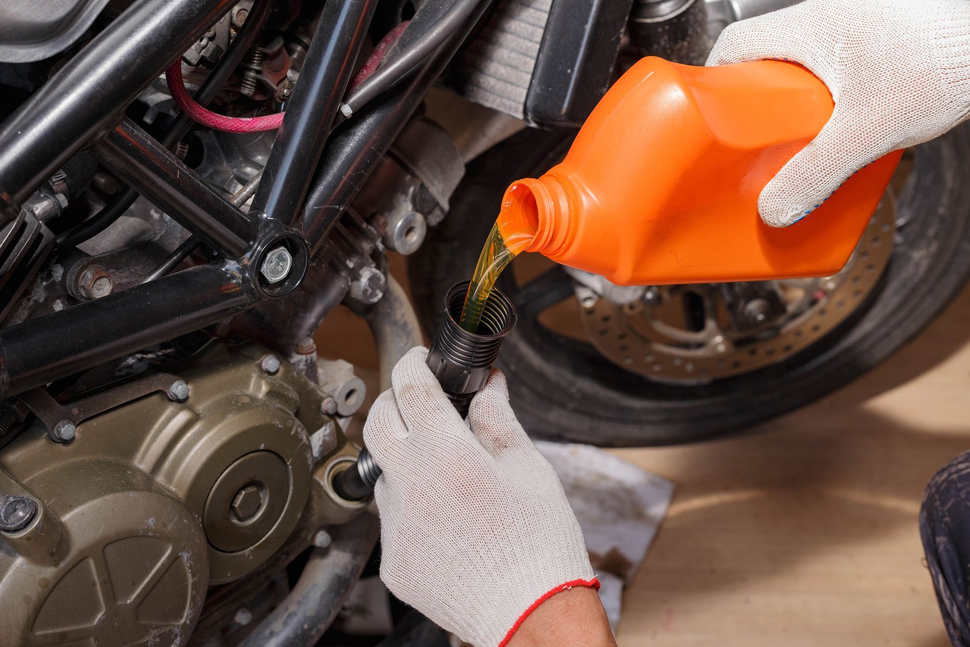 Person pouring oil from orange container into motorcycle engine.